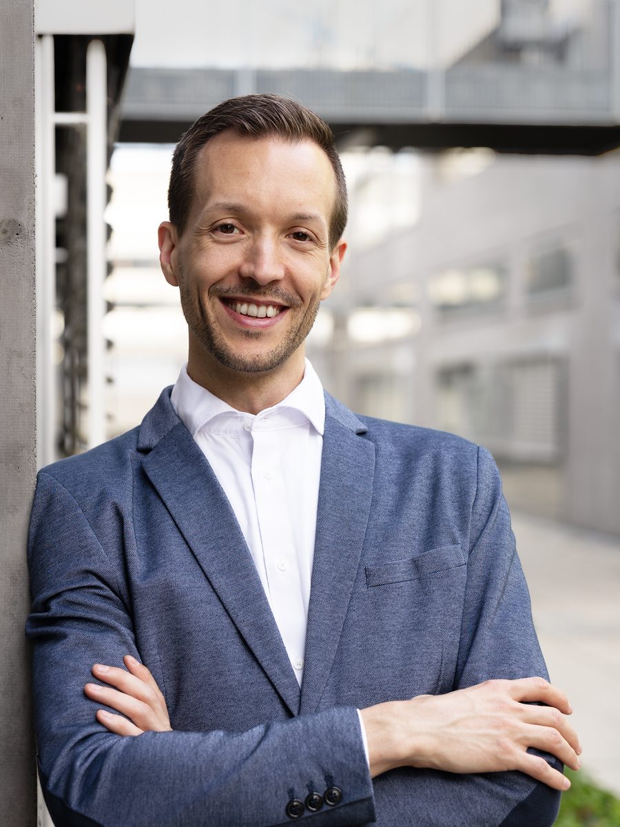 Stefan Kirchsteiger, smiling, arms folded, leaning against a concrete pillar.